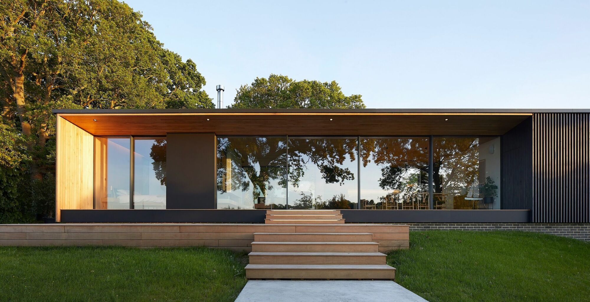 Une maison moderne avec de grandes baies vitrées, une façade en bois et une terrasse couverte